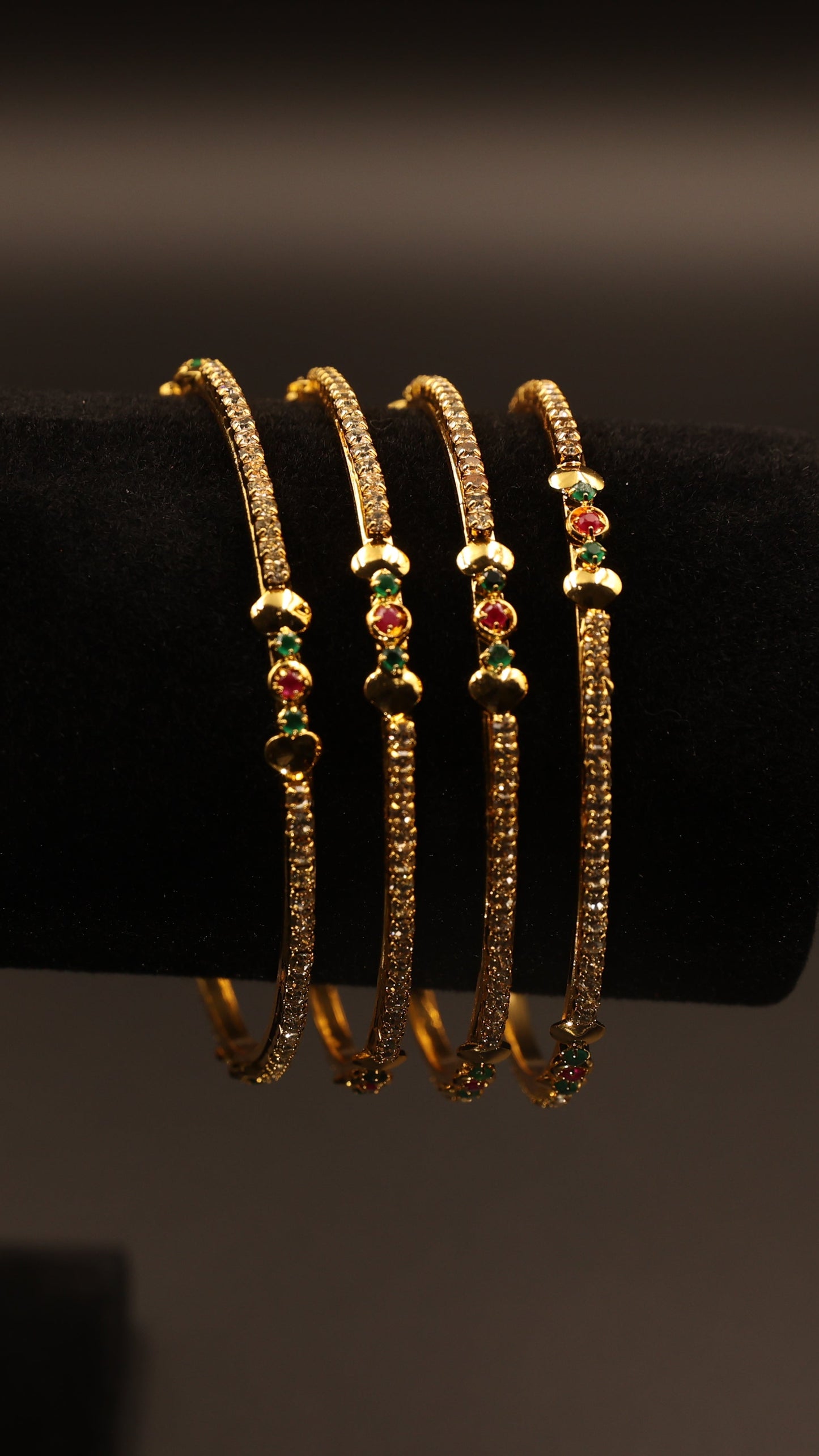 Set of gold bangles with small stones on a black stand against a dark background
