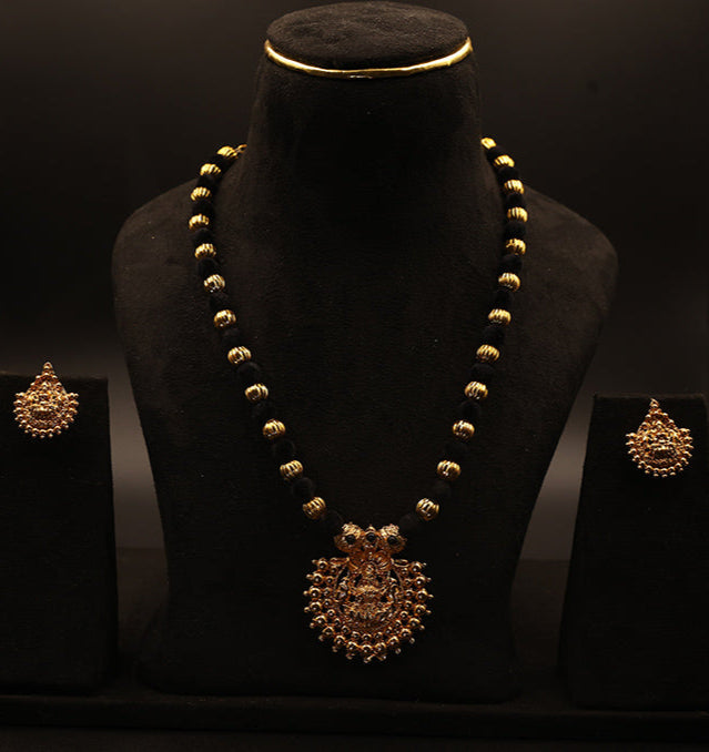 Gold necklace and earrings on a black stand against a dark background