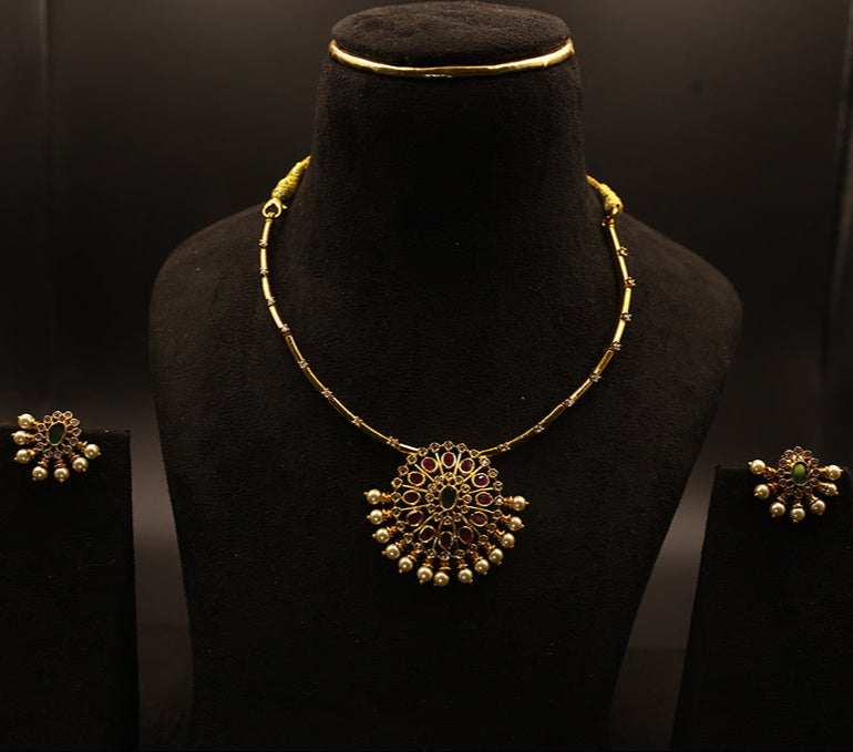 Gold necklace and earrings on a black mannequin against a dark background