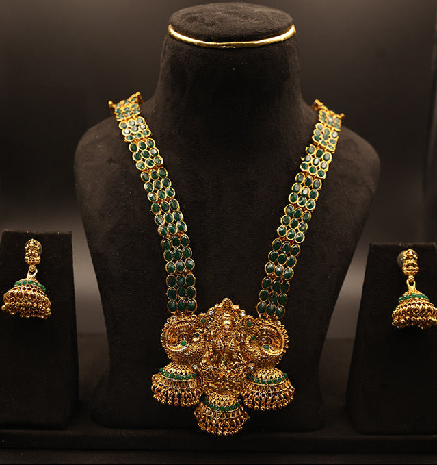 Gold necklace with green gemstones on a black mannequin bust, accompanied by matching earrings on black stands.