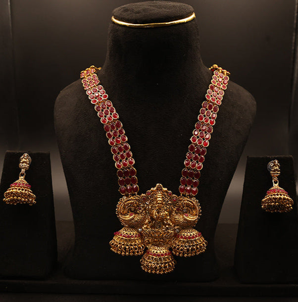 Gold and red jewelry set on a black mannequin with a dark background