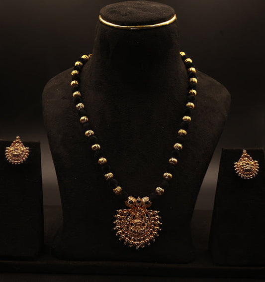 Gold necklace and earrings on a black stand against a dark background