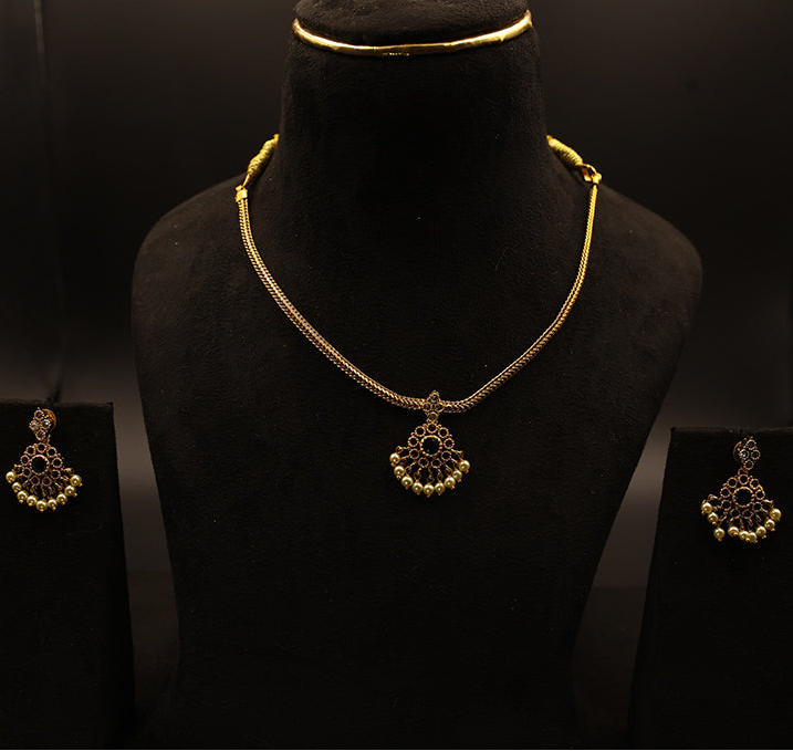 Gold necklace and earrings on a black mannequin against a dark background