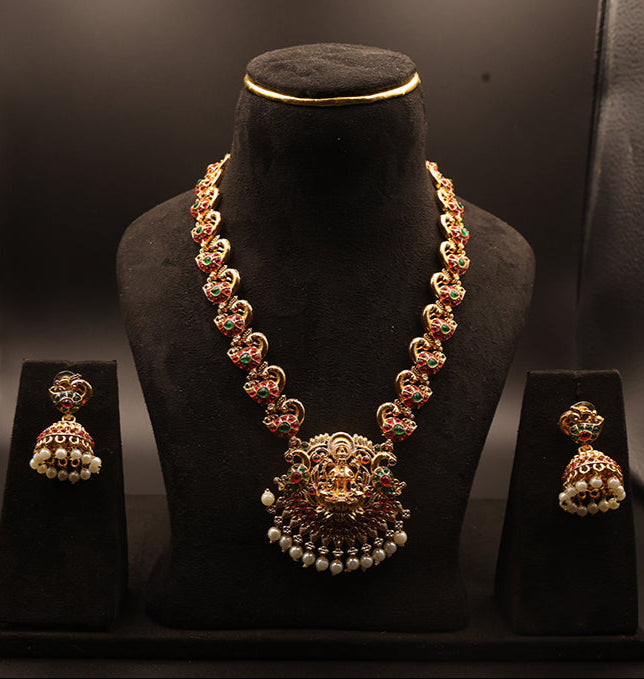 Gold necklace and earrings set on a black stand against a dark background