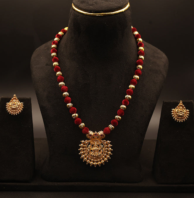 Gold necklace with red beads on a black stand against a dark background