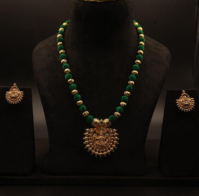Green and gold necklace with matching earrings on a black mannequin against a dark background