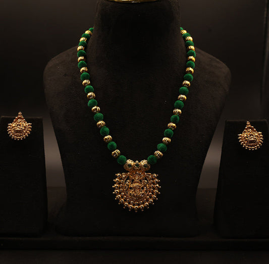 Green and gold necklace with matching earrings on a black mannequin against a dark background
