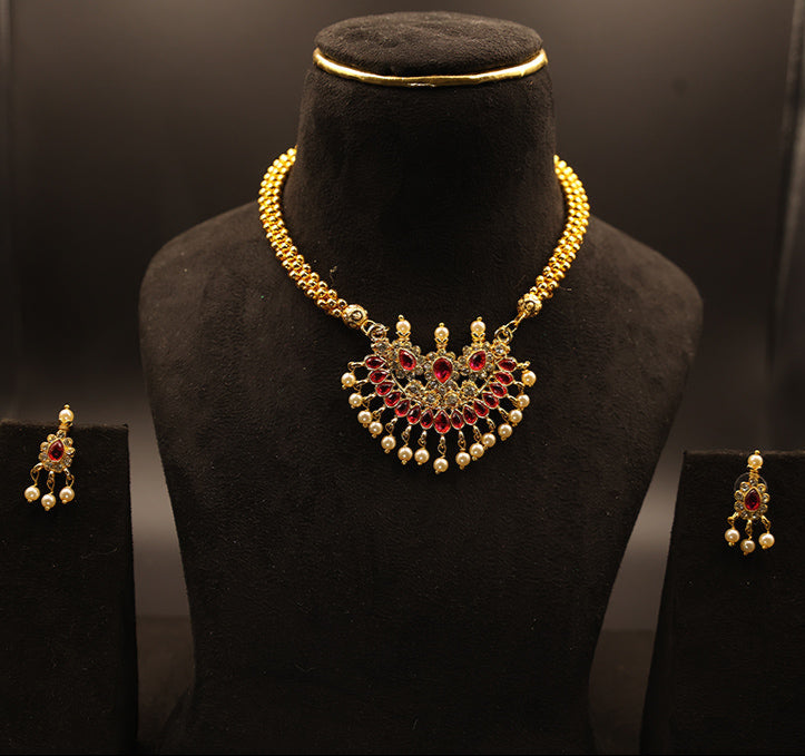 Gold necklace with red Stones on a black mannequin bust, with matching earrings on either side.
