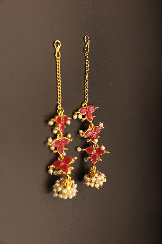 Ornate earrings with red stones and gold chains on a dark background