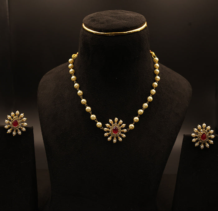 Pearl necklace with red gemstones on a black mannequin bust against a dark background