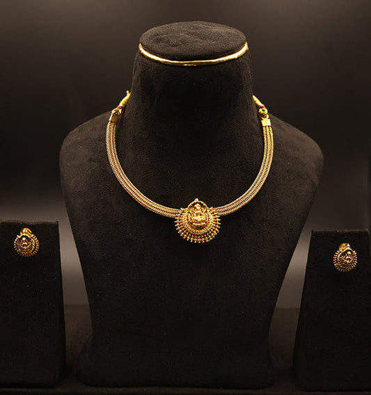 Gold necklace and earrings on a black mannequin bust against a dark background